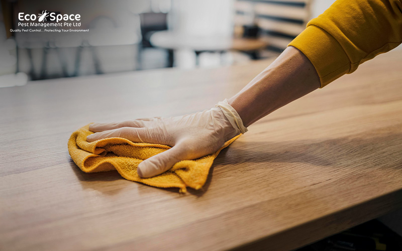 Person in gloves cleaning a wooden table with a cloth
