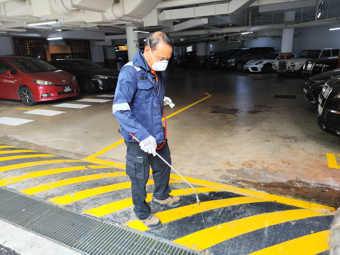 Pest control technician performing mosquito larviciding treatment along a drainage area in a commercial carpark.